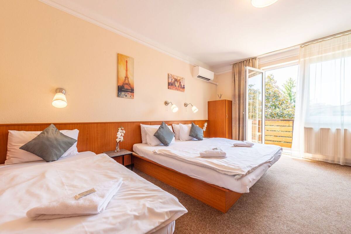 Habitación de hotel con dos camas, un cabecero de madera, un ventanal grande con cortinas y una obra de arte en la pared.
