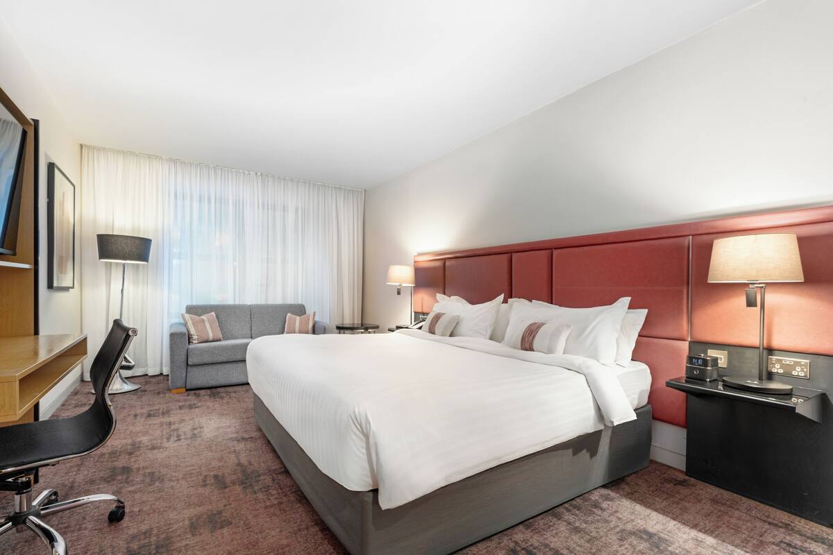Una habitación de hotel con una cama grande, un escritorio, una silla, un sofá y una mesita de noche con lámparas.