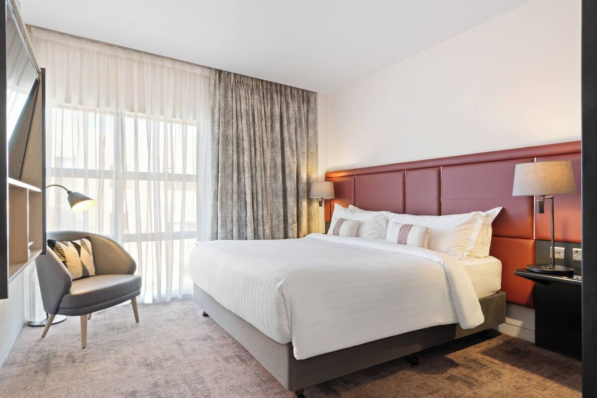 Una habitación de hotel con una cama grande, una silla, una mesita de noche y una lámpara.