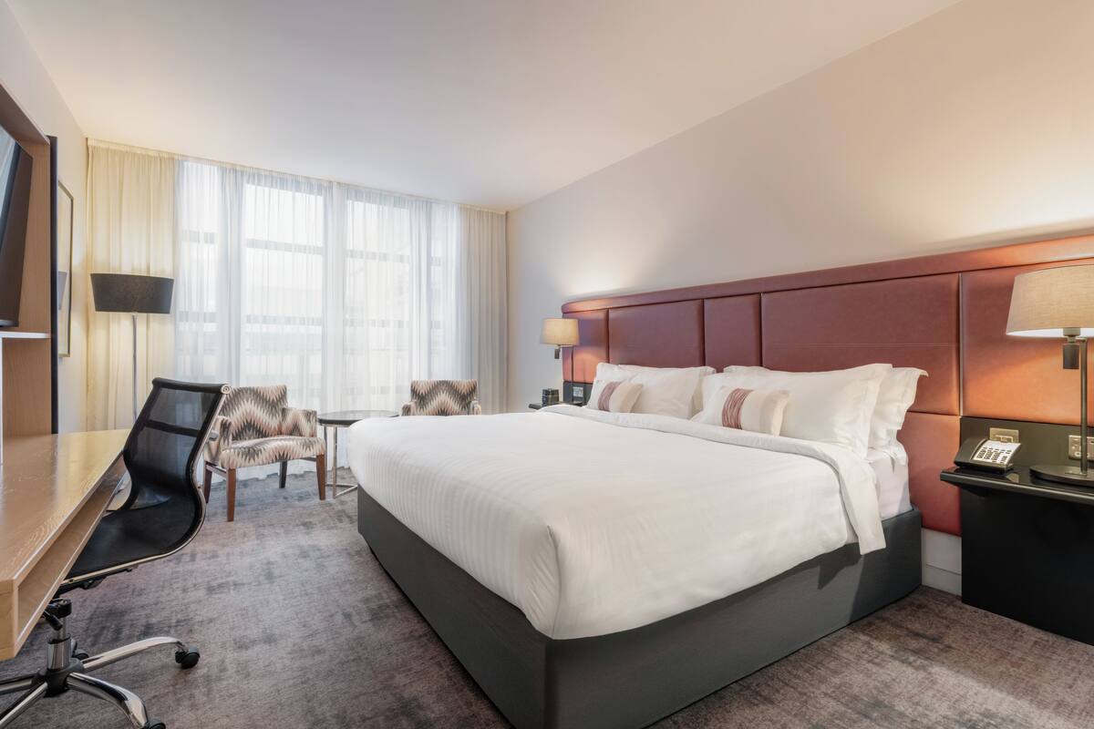 Una habitación de hotel con una cama grande, un escritorio, una silla y un televisor.