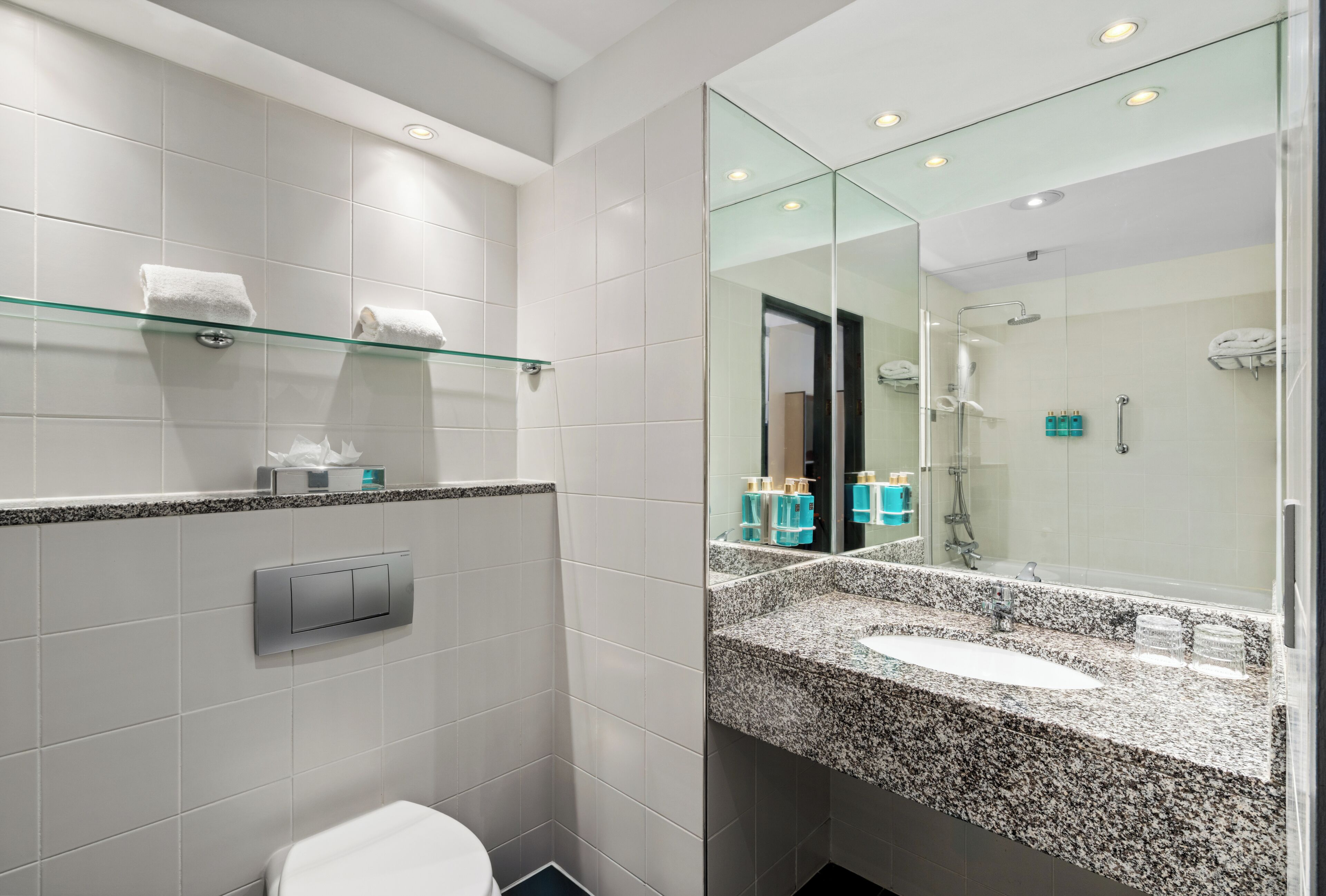 Un baño moderno con lavamanos de encimera de granito, cabina de ducha de vidrio y retrete.