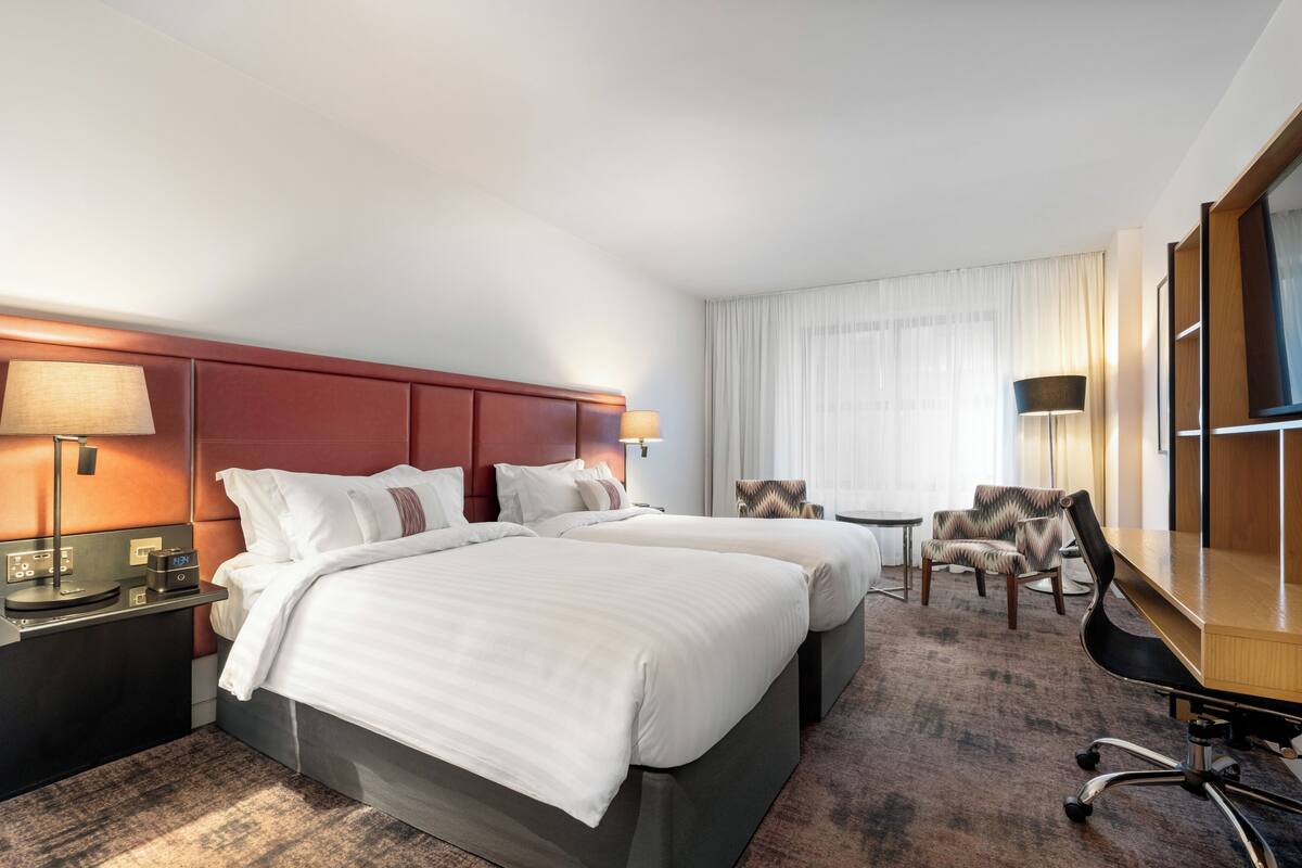 Una habitación de hotel con dos camas, un escritorio, una silla y un televisor.