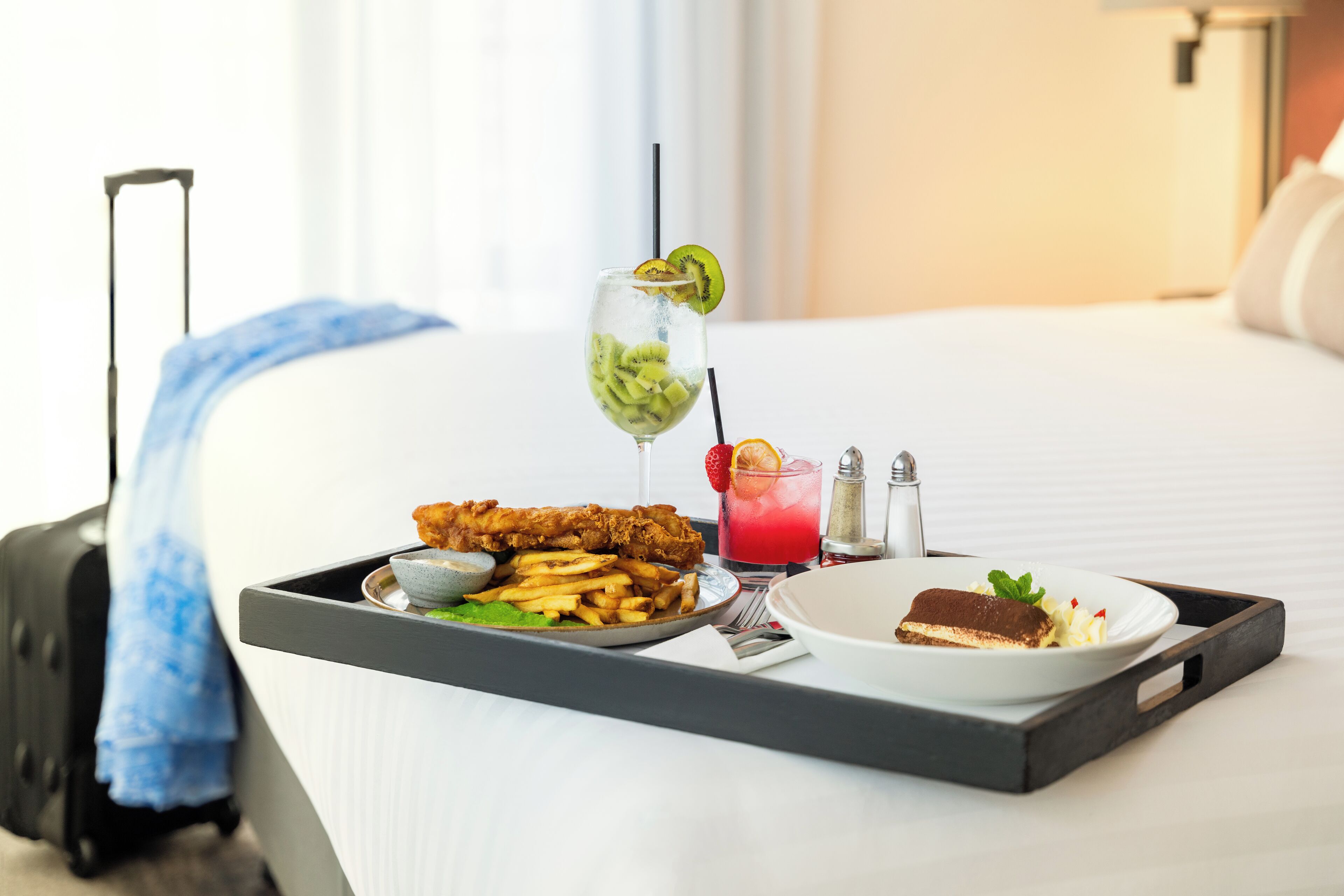A tray with a meal consisting of fried fish, fries, a dessert, and a drink with a slice of kiwi and a straw.