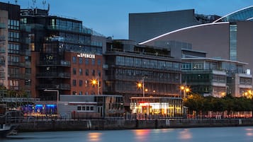 A modern urban building with a prominent 'The Spencer' sign, a glass facade, and a waterfront setting.