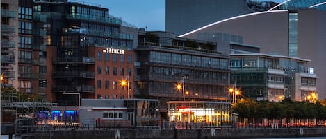 Un moderno edificio urbano con un llamativo letrero 'The Spencer', fachada de vidrio y ubicación frente al agua.