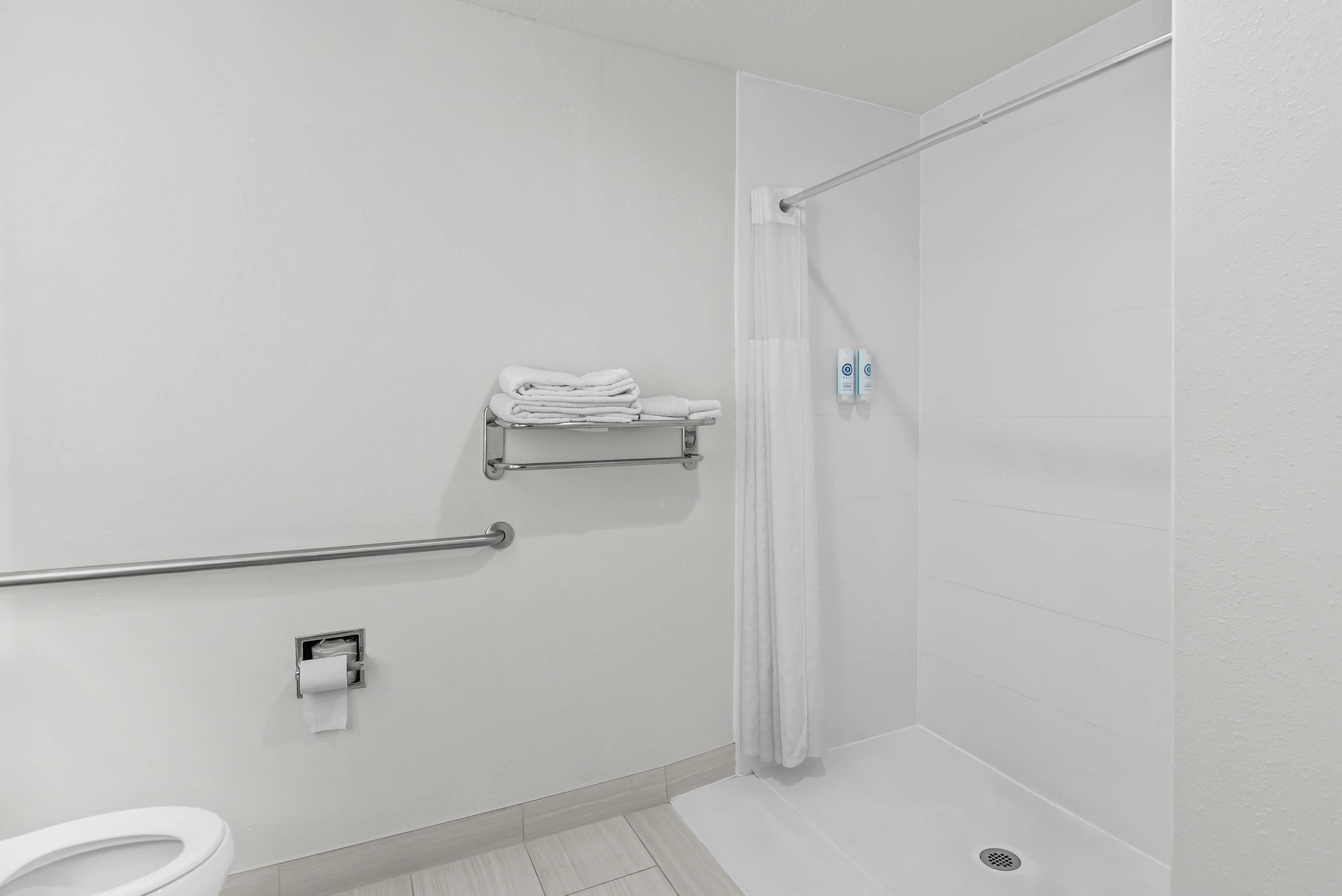 Une salle de bain blanche équipée d’une douche, de toilettes, d’un porte-serviettes et d’une barre d’appui.