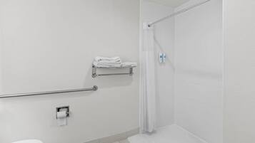 Une salle de bain blanche équipée d’une douche, de toilettes, d’un porte-serviettes et d’une barre d’appui.