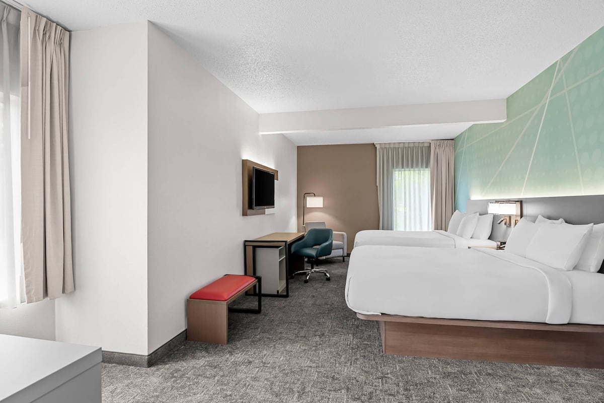 A hotel room with a bed, desk, chair, and a TV.