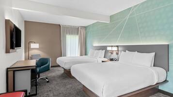 A hotel room with two beds, a desk, a chair, a TV, and a window with curtains.