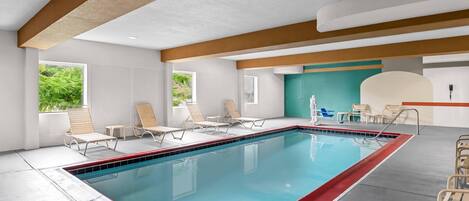 Una piscina con sillones de descanso, una pared azul verdoso y una viga de techo de madera.