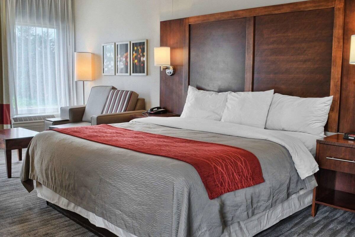 A hotel room with a large bed, a desk, a chair, a lamp, and artwork on the wall.