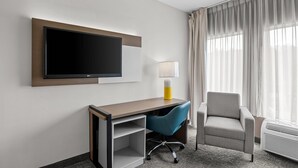 A hotel room with a flat-screen TV mounted on the wall, a desk with a chair, a lamp, and a window with curtains. - Comfort Inn Ruther Glen near Kings Dominion (Ruther Glen)