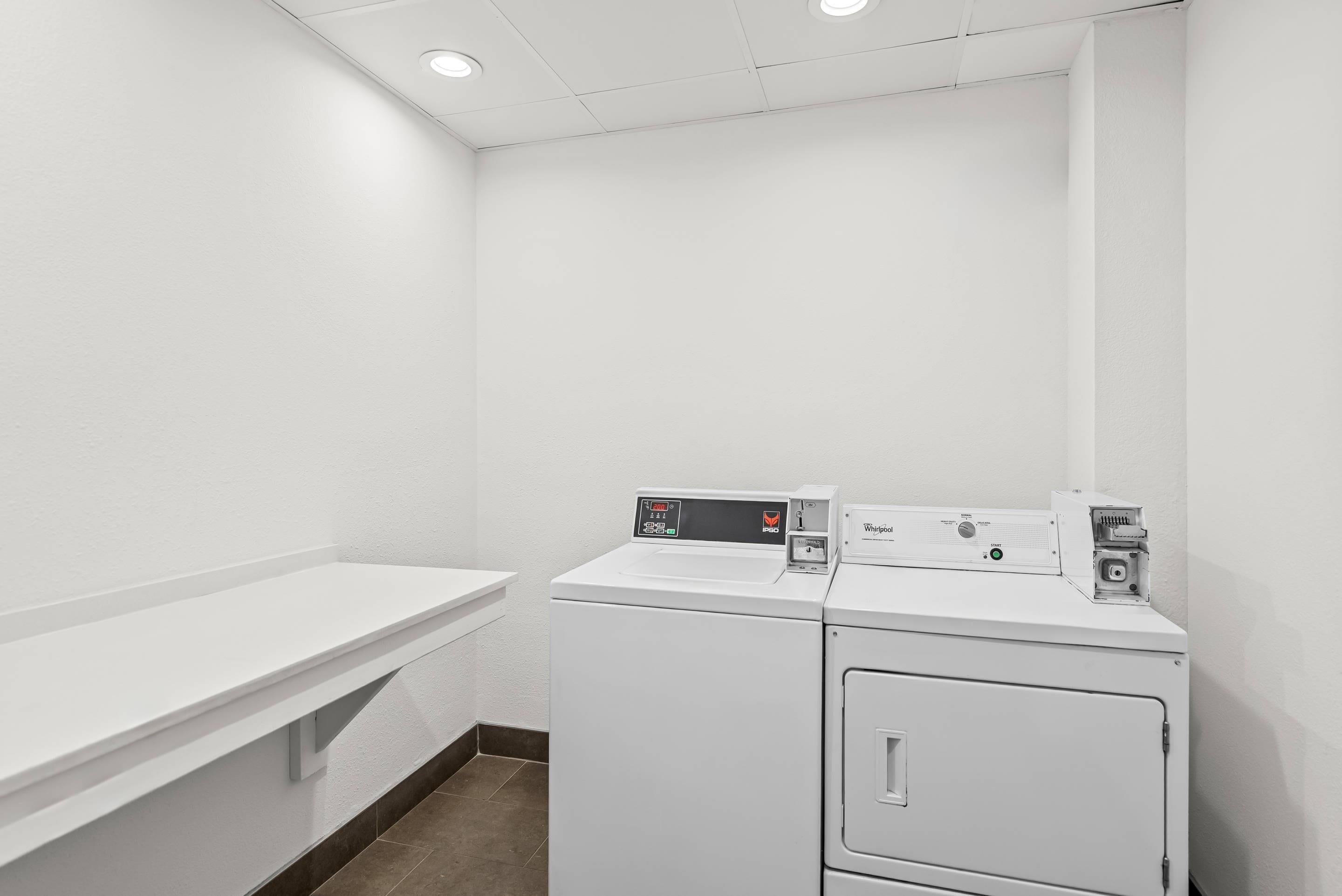 A laundry room with a white washing machine and dryer, a white sink, and a white countertop.