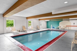 A swimming pool with lounge chairs, a teal wall, and a wooden ceiling beam.
