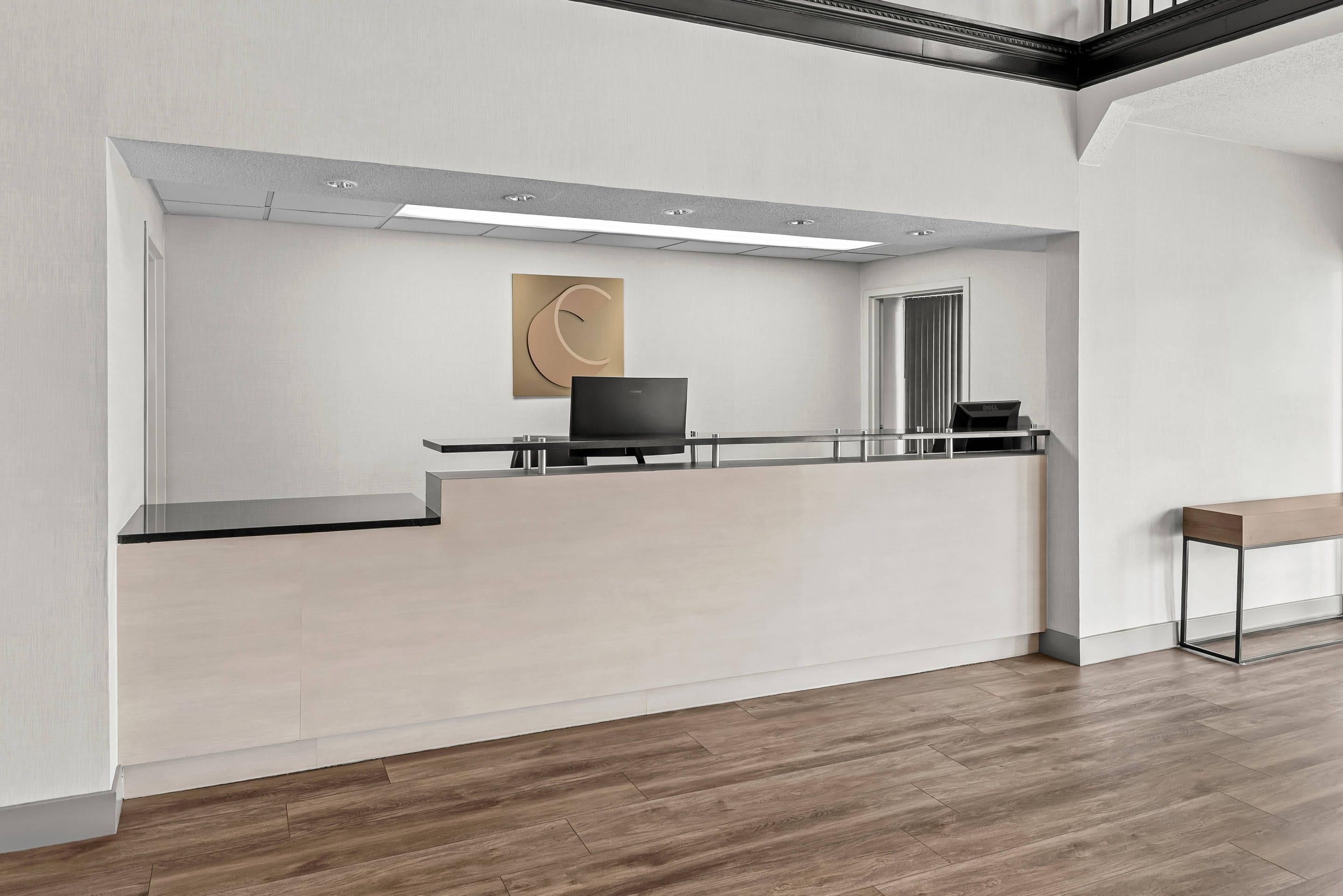 A reception desk with a laptop, a framed abstract artwork, and a mirror on the wall.