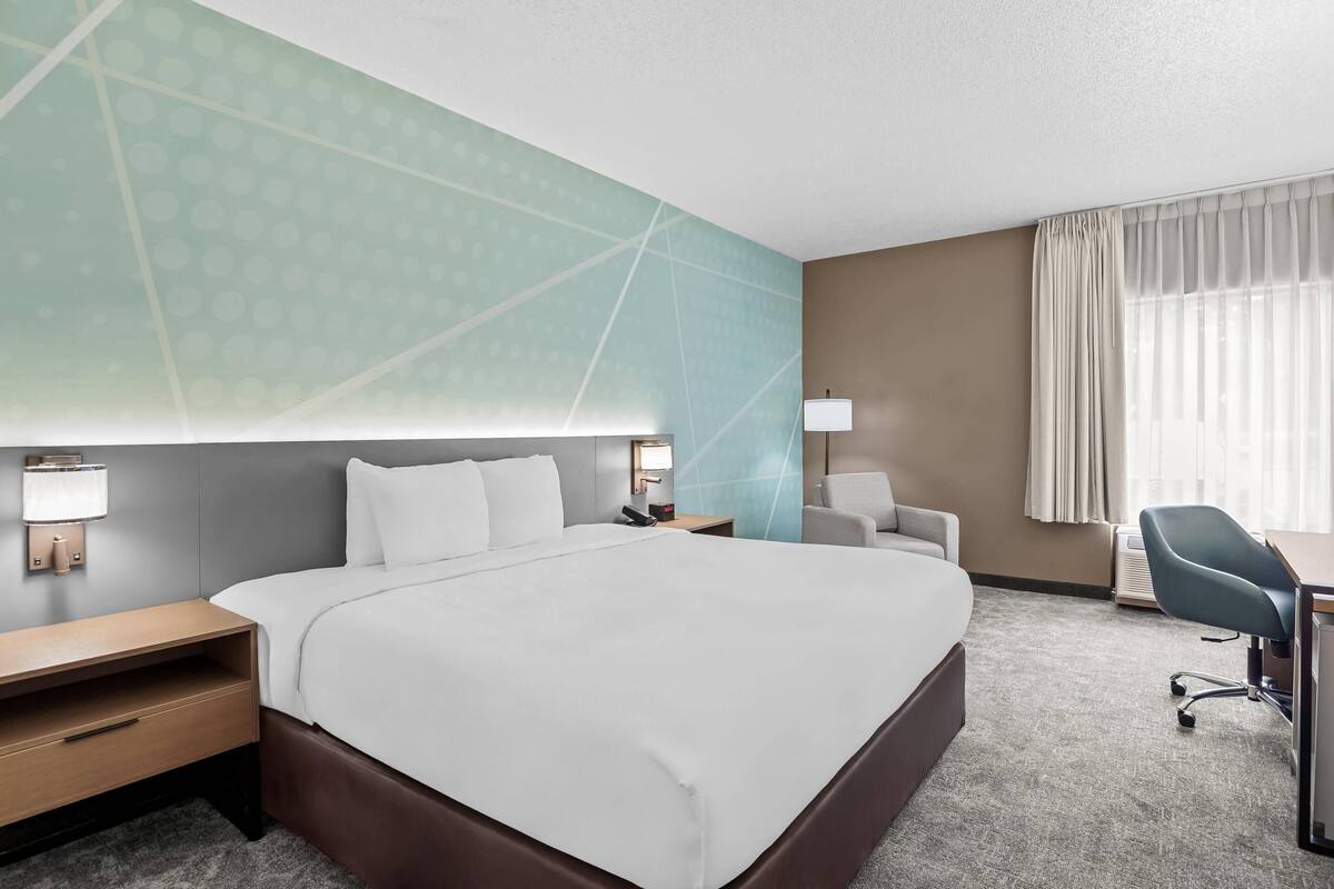 A hotel room with a large bed, bedside tables, a desk, a chair, and a window with curtains.