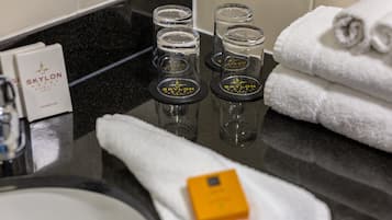 Ein Badezimmer-Waschtisch mit Waschbecken, einem Handtuch, einer Shampoo-Flasche und drei Glasbehältern mit dem Schriftzug 'Skylon'.