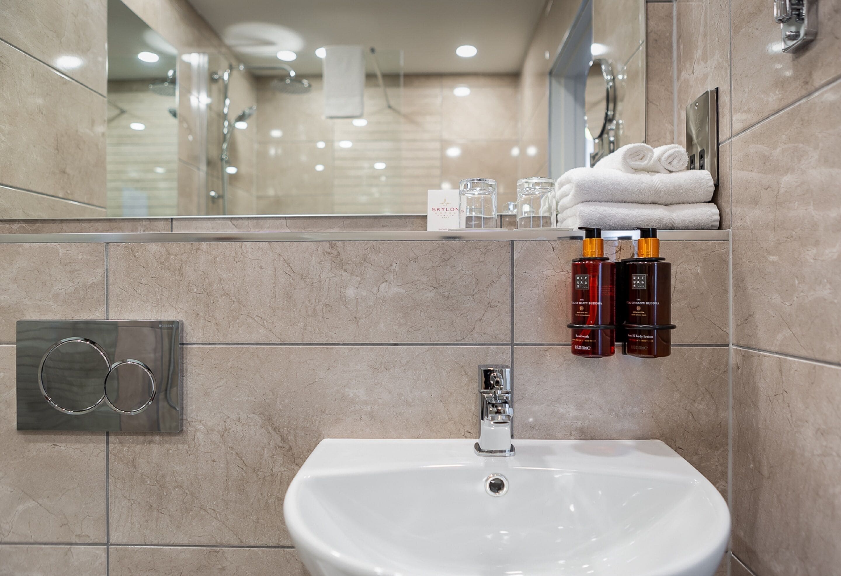 A modern bathroom with a white sink, a towel rack with folded towels, and two bottles of shampoo.