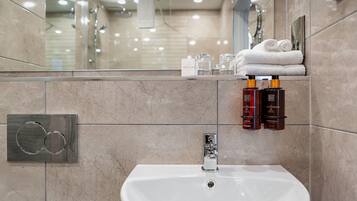 A modern bathroom with a white sink, a towel rack with folded towels, and two bottles of shampoo.
