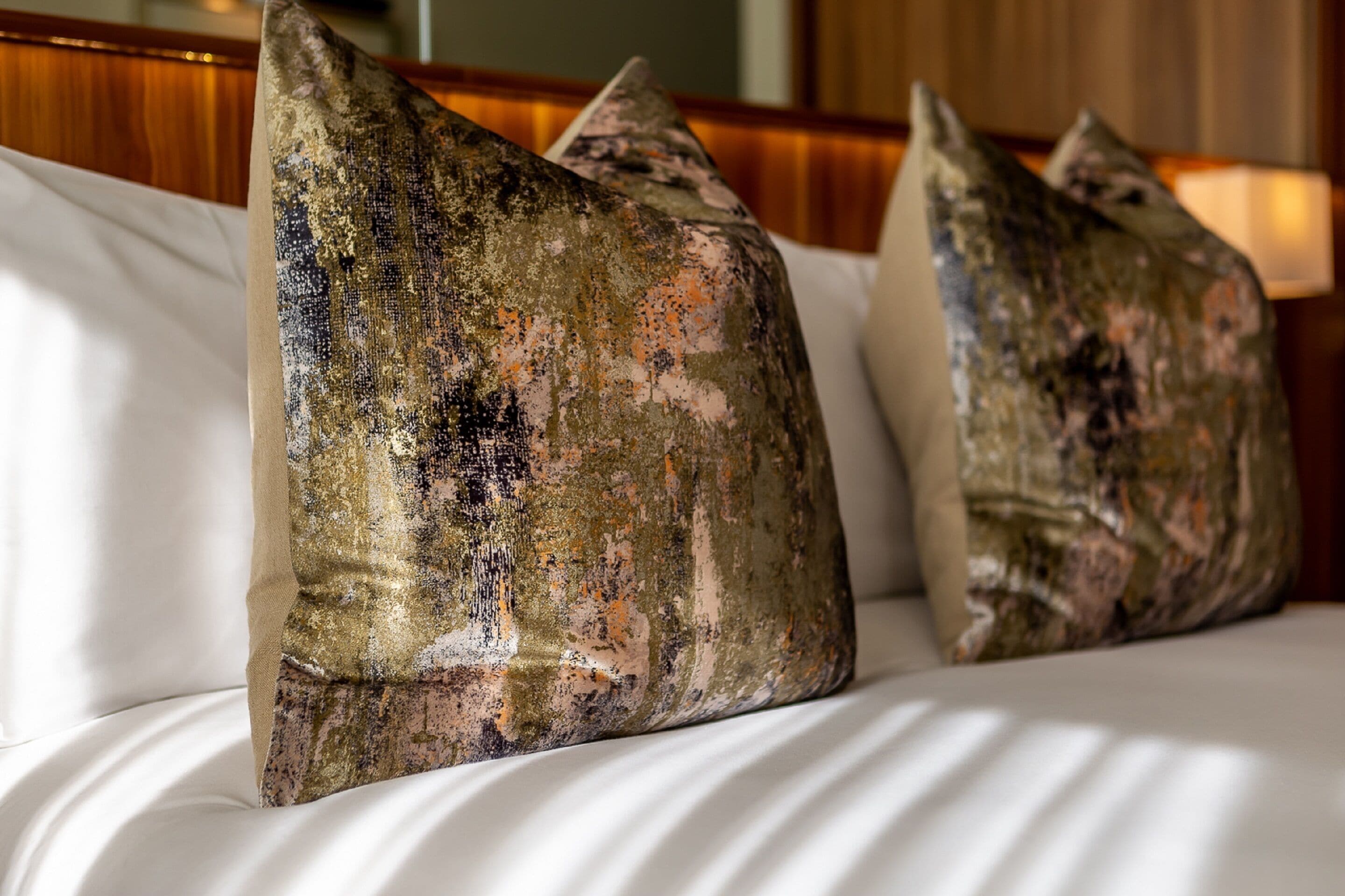 A bed with white linens and two decorative pillows with a camouflage pattern.