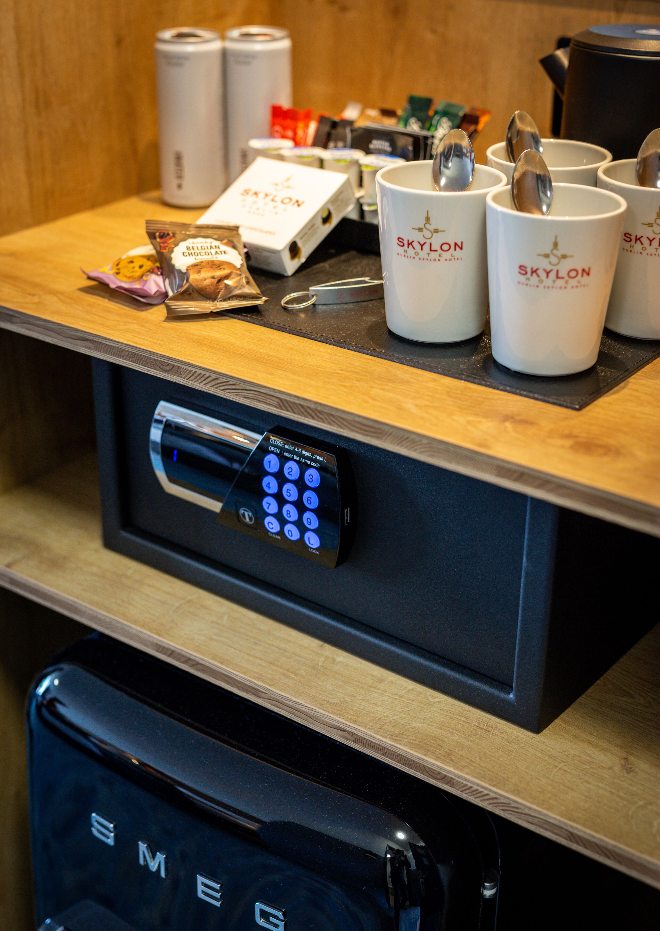 A hotel reception area with a digital keypad for room access, branded SkyLON mugs, and a bag of Belgian chocolate cookies.