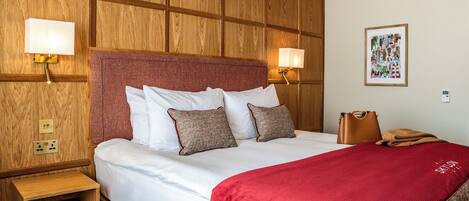 Ein Hotelzimmer mit einer Holzwand, einem großen Bett mit weißen Leinentüchern, einer roten Tagesdecke und zwei Wandlampen.
