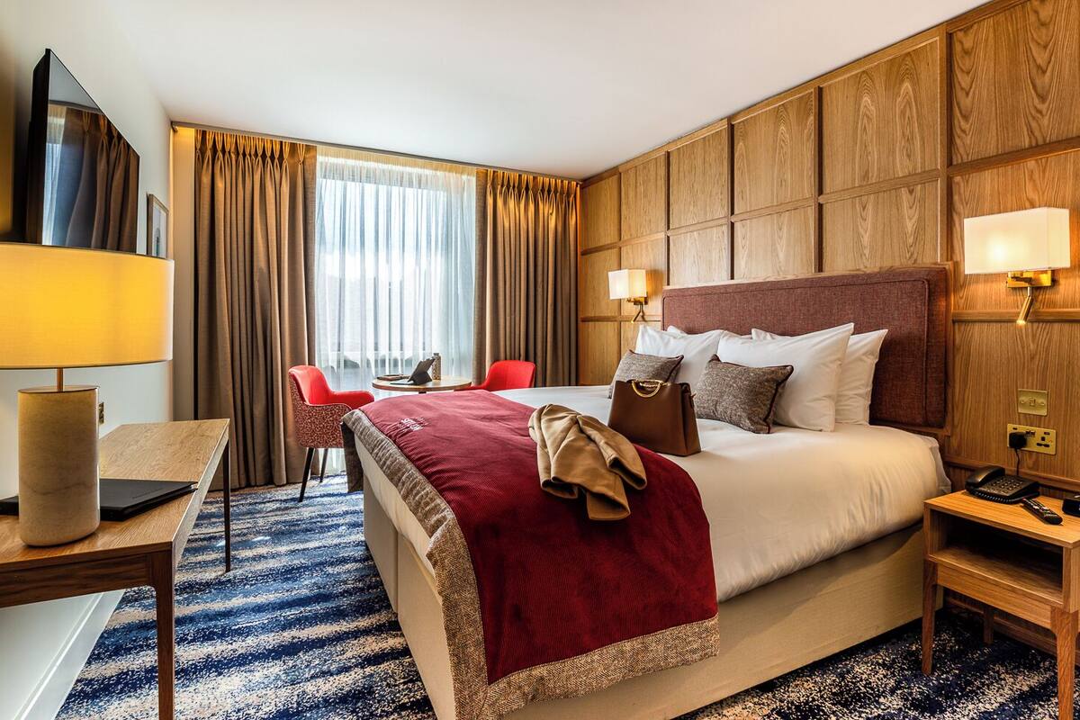 Habitación de hotel con cama, mesitas de noche, escritorio, silla y ventana con cortinas.