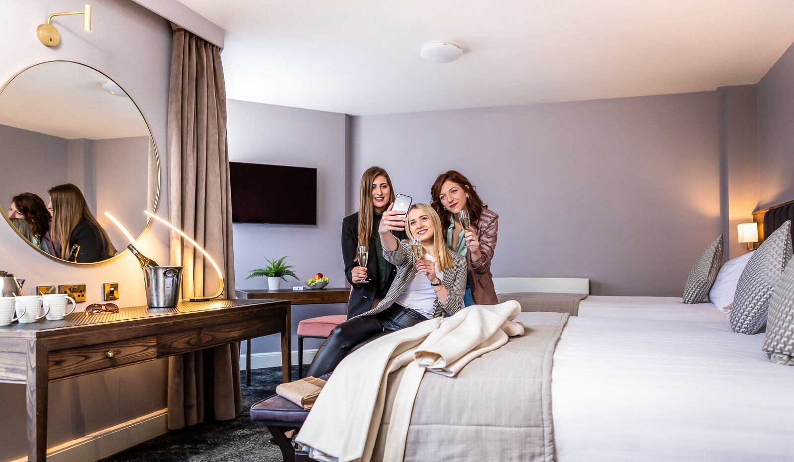 Ein Hotelzimmer mit Bett, Nachttisch, Spiegel und einem an der Wand befestigten Flachbildfernseher.