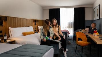 Habitación de hotel con cama, escritorio y silla. Hay un reloj en la pared y una botella de vino sobre la mesita de noche.
