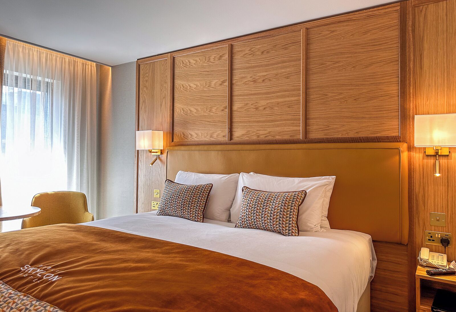 Une chambre d’hôtel avec un grand lit, deux oreillers, une table de chevet avec une lampe et une chaise.