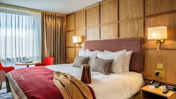 Una habitación de hotel con una cama grande, dos lámparas de noche, una mesita de noche con un teléfono y un reloj, una silla roja y una pequeña mesa con un libro.