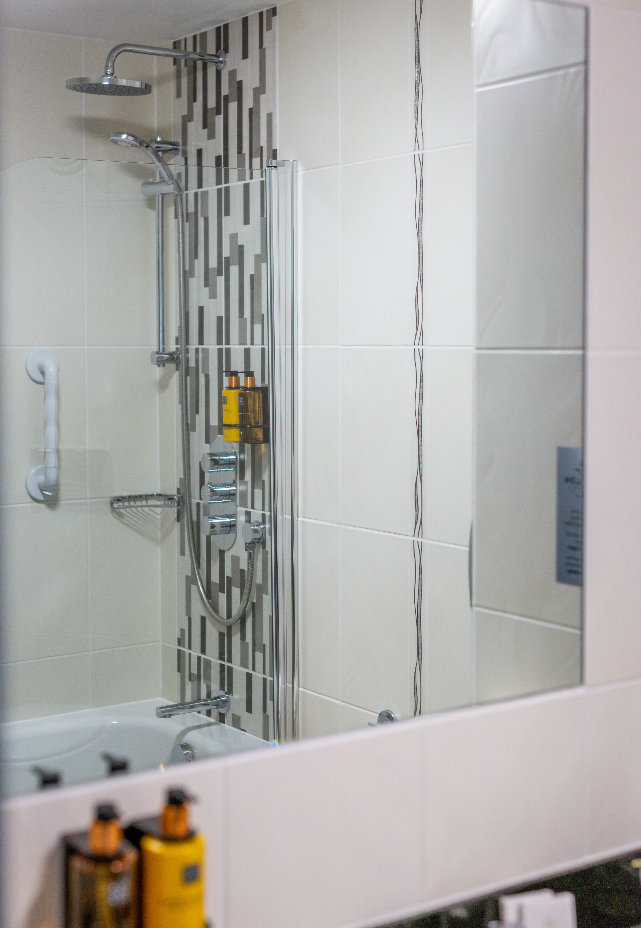 Ein Badezimmer mit Duschkabine aus Glas, einer Badewanne und einem Spiegel, der den Raum reflektiert.
