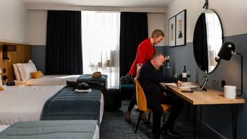 Una habitación de hotel con dos camas, un escritorio con una computadora portátil, un espejo y una ventana con cortinas.