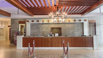A hotel reception area with a wooden reception desk, a chandelier, and a stone-patterned floor.