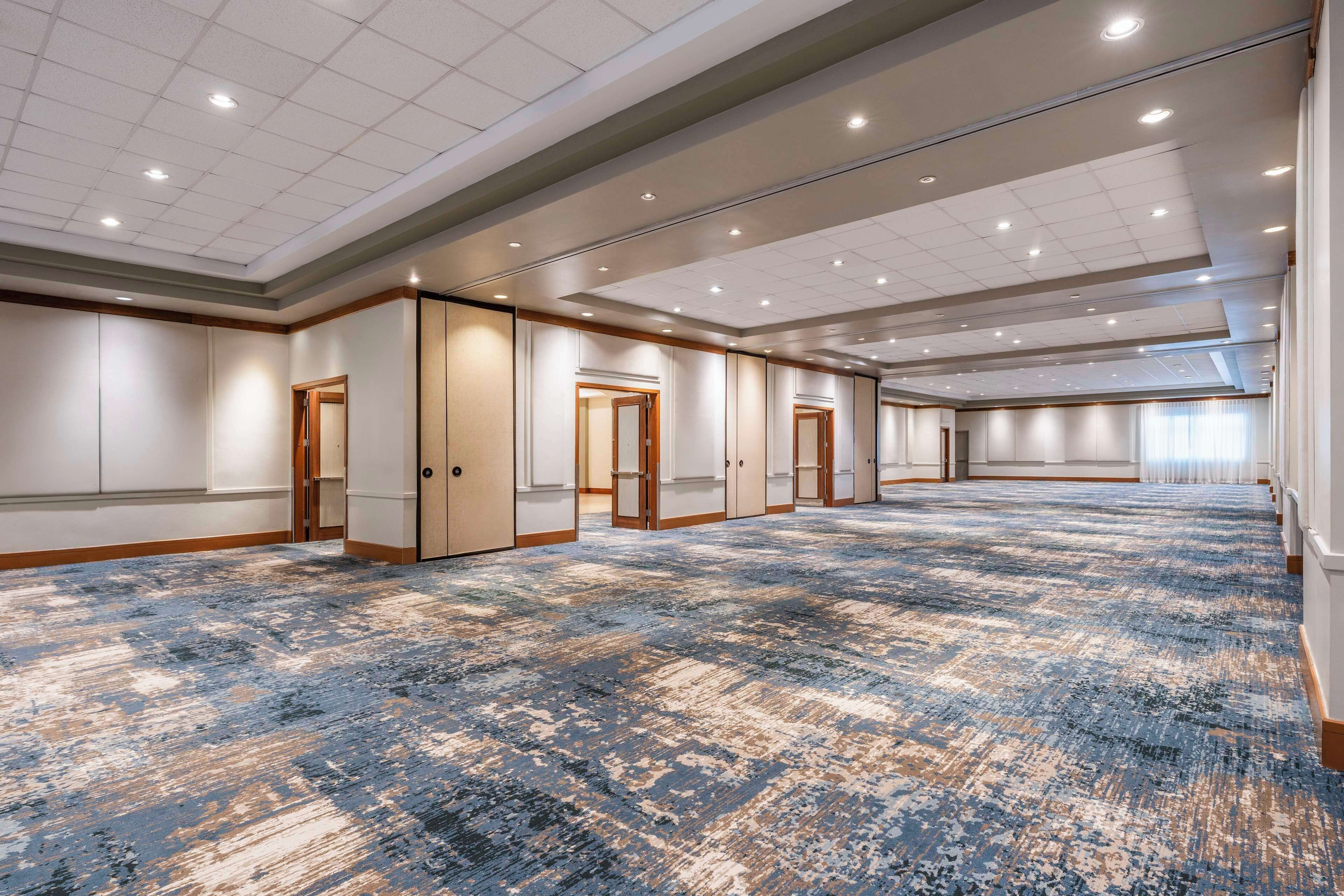 A large, well-lit conference room with a patterned carpet, multiple doors, and a high ceiling with recessed lighting.