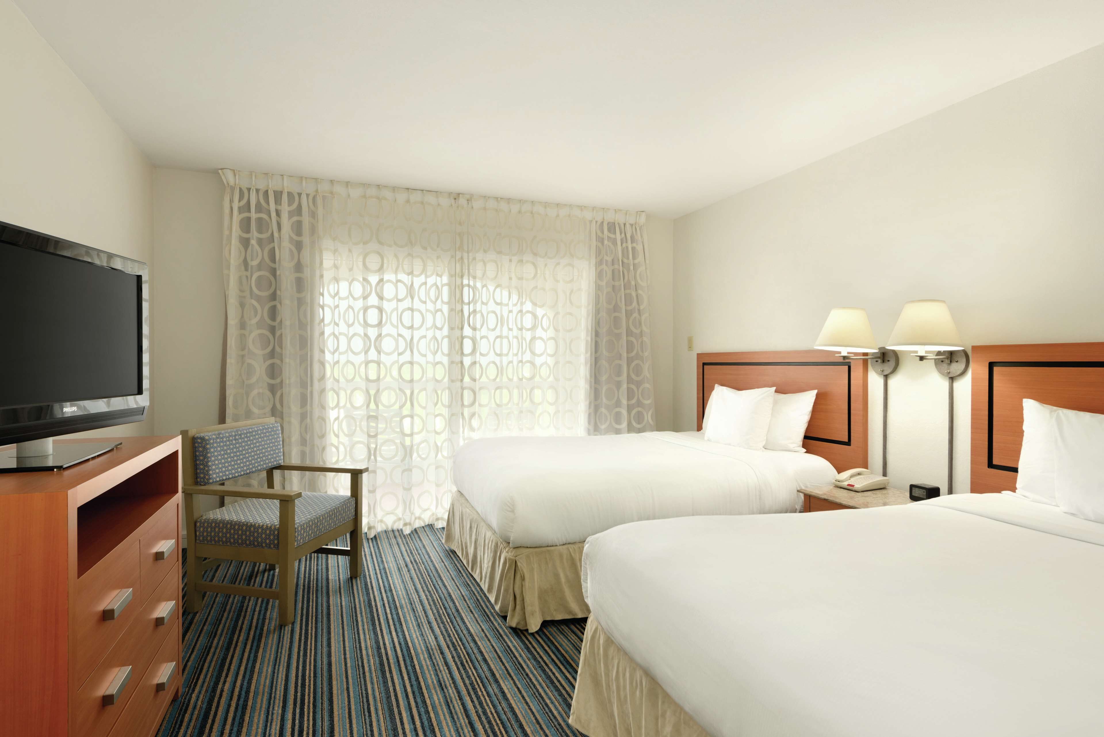 A hotel room with two beds, a TV, a desk with a lamp, and a chair.