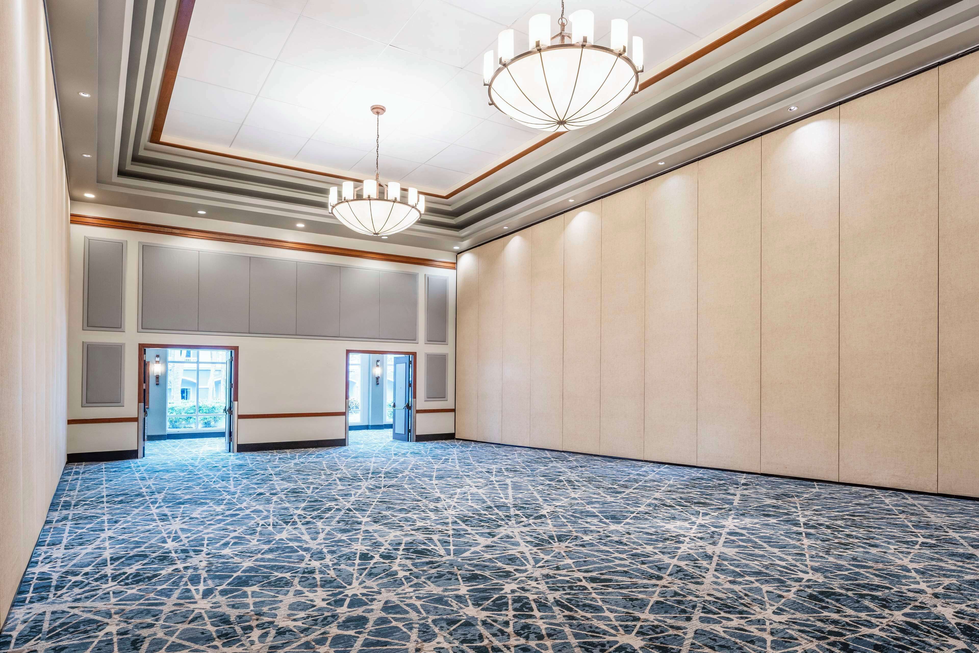 A spacious conference room with a patterned floor, two chandeliers, and a view through a doorway to an outdoor area.