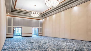 Una amplia sala de conferencias con piso estampado, dos candelabros y vistas a un espacio exterior a través de un vano.