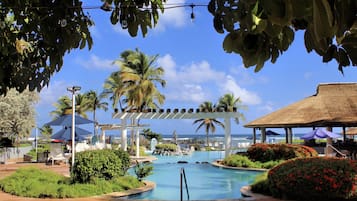 Zona de piscina en un resort, con palmeras, sombrillas y vista al océano.