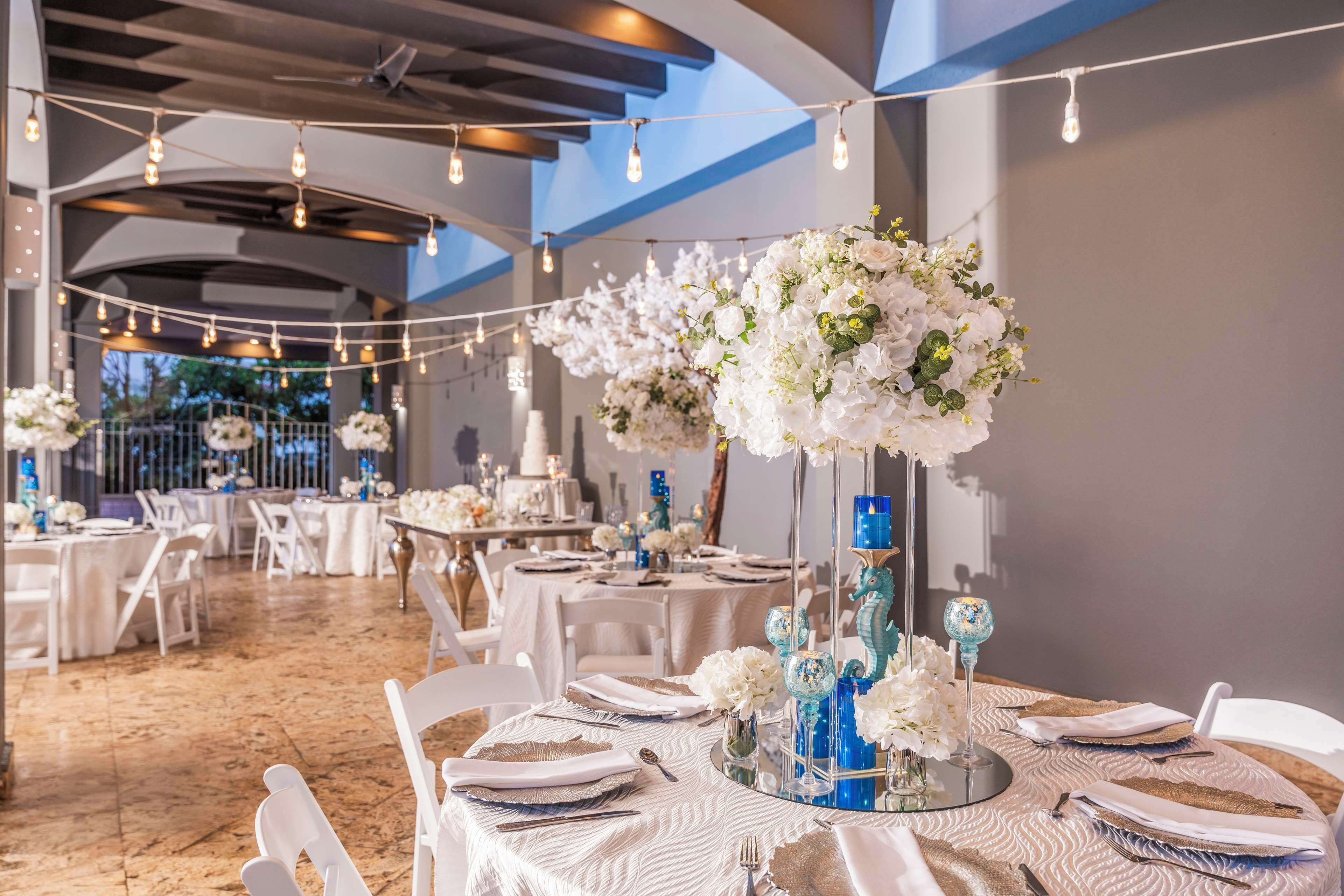 A banquet hall with round tables, white tablecloths, and floral centerpieces.