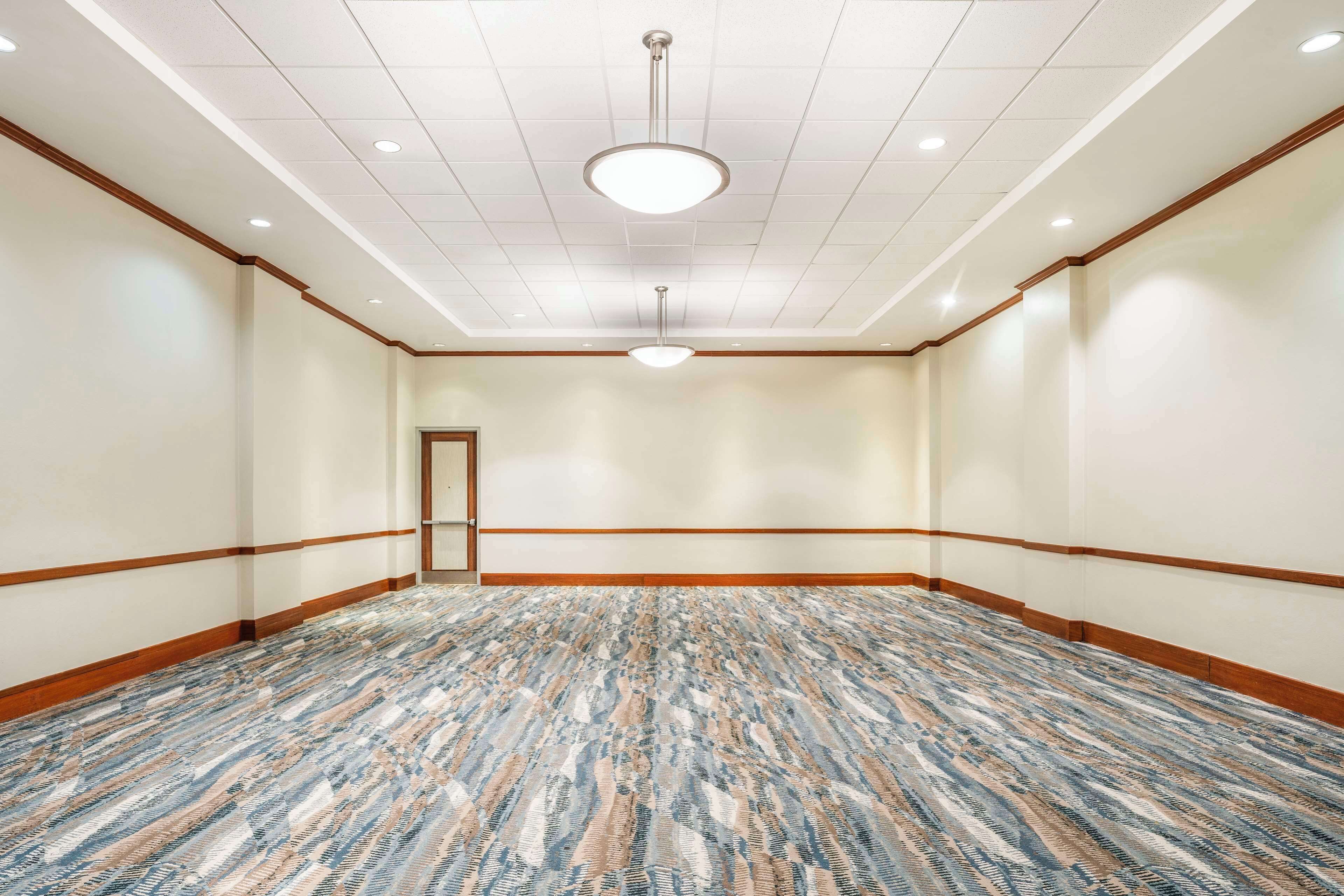 Un amplio salón de conferencias vacío con alfombra estampada, molduras de madera y luces empotradas en el techo.