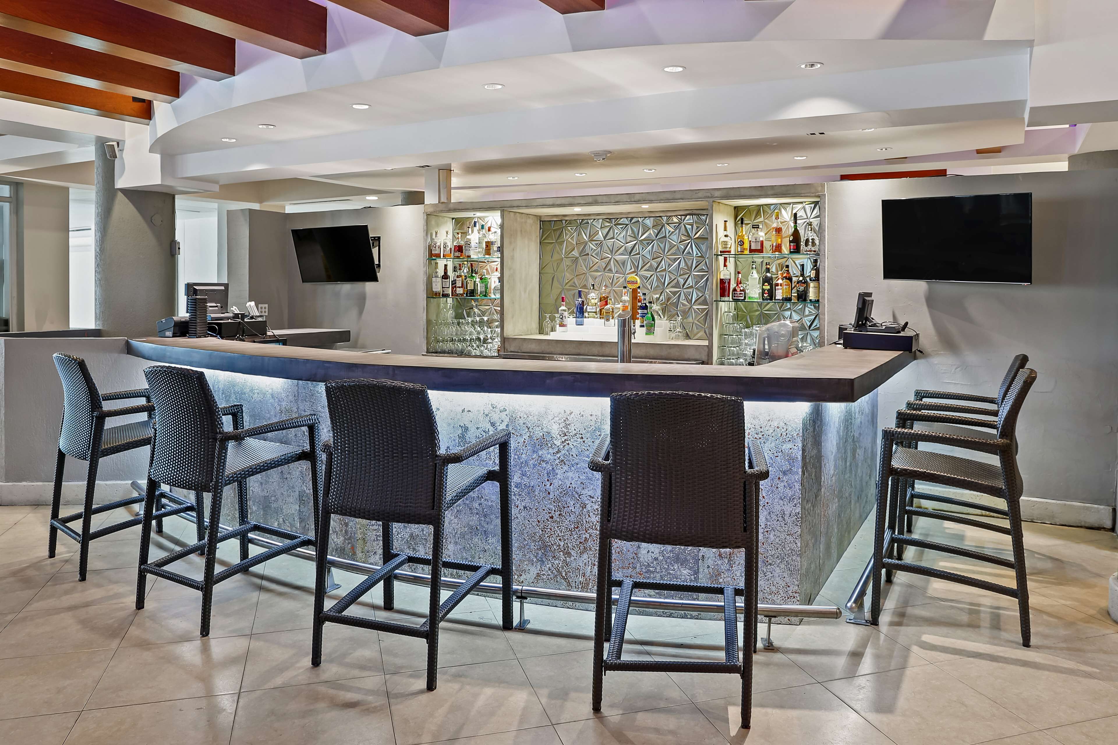 Zona de bar moderna con una barra central, taburetes, una partición de vidrio y un televisor montado.