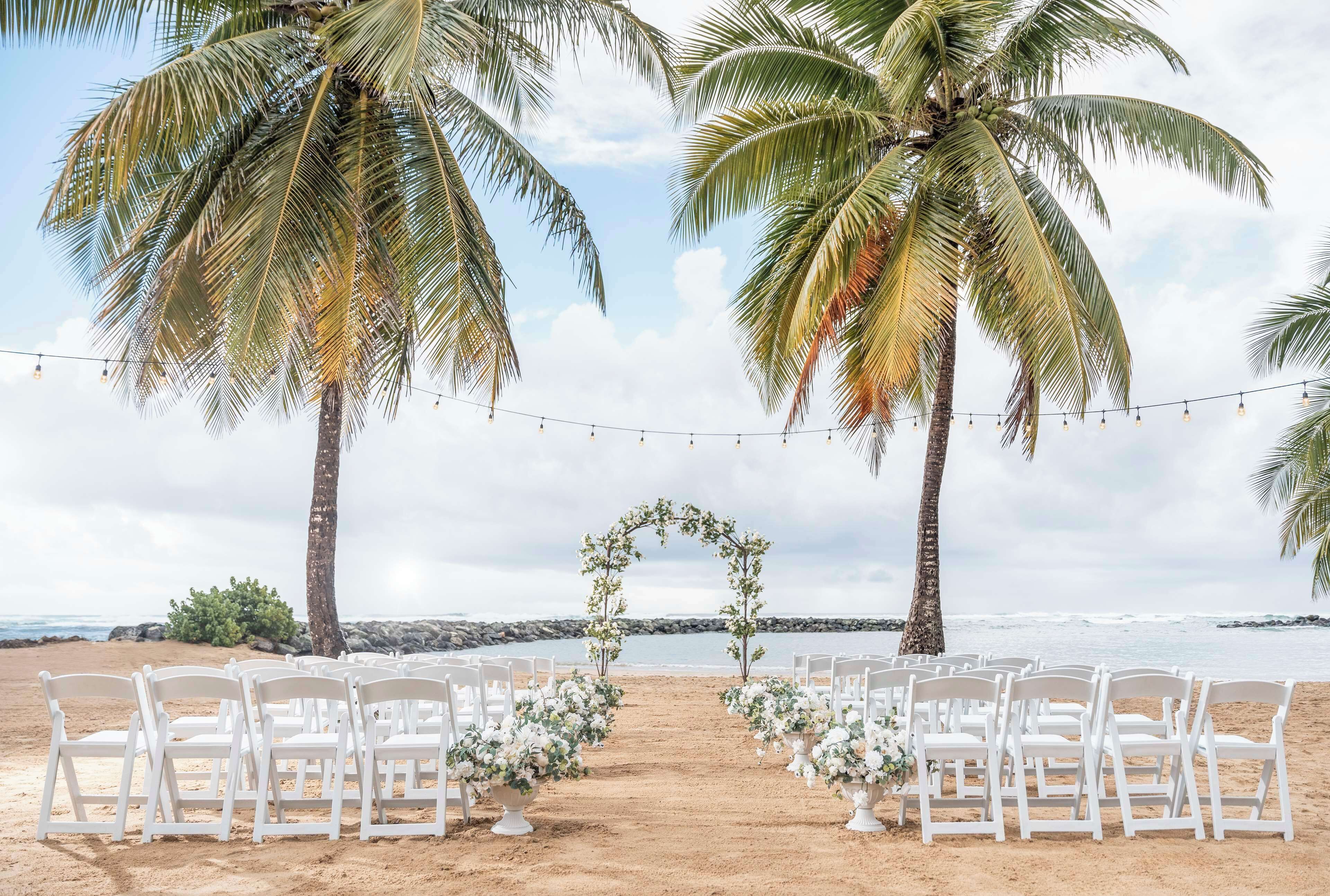 Decoración de boda en la playa con sillas blancas y un arco floral.