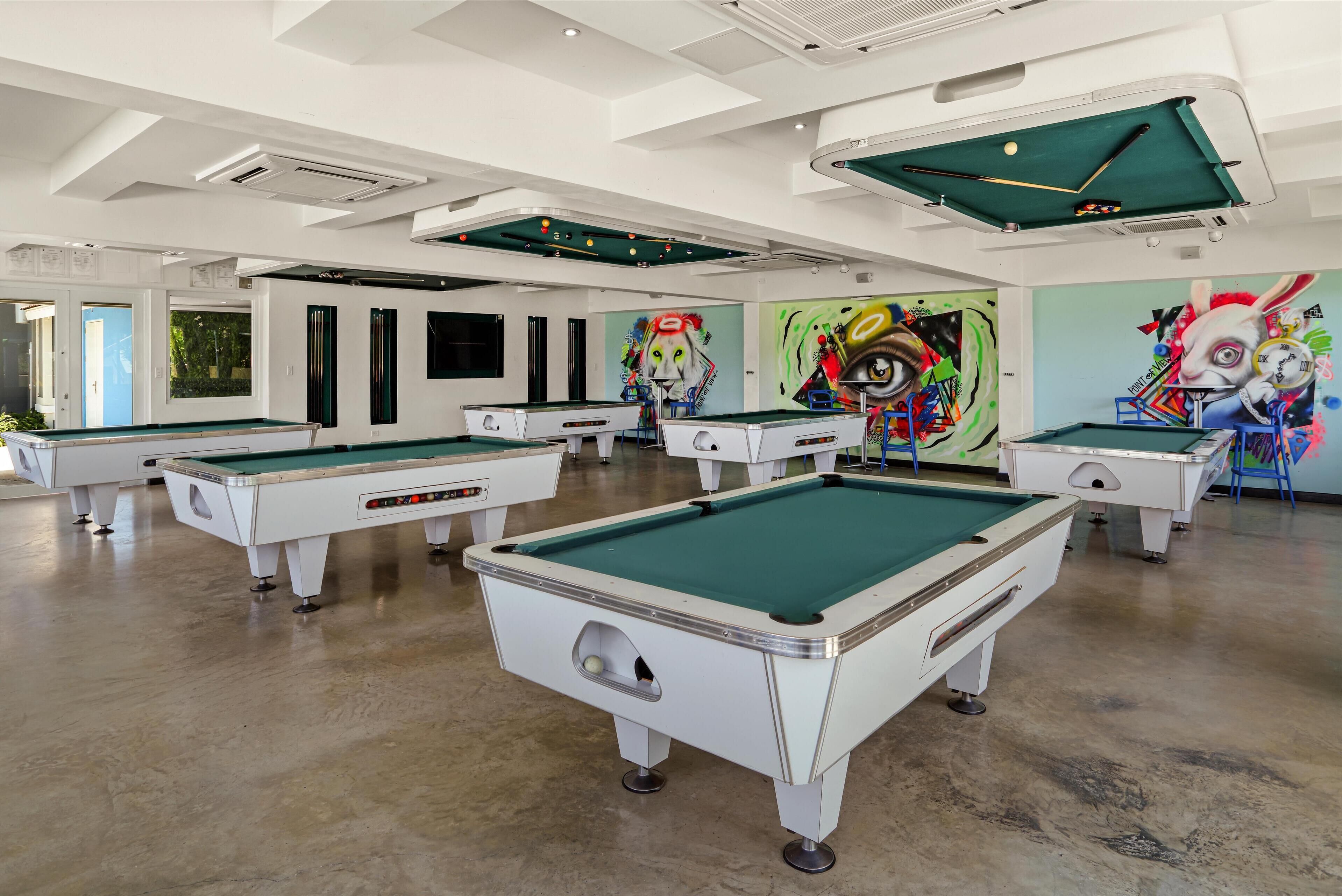 Een poolzaal met meerdere pooltafels, plafondverlichting en kleurrijke muurschilderingen.