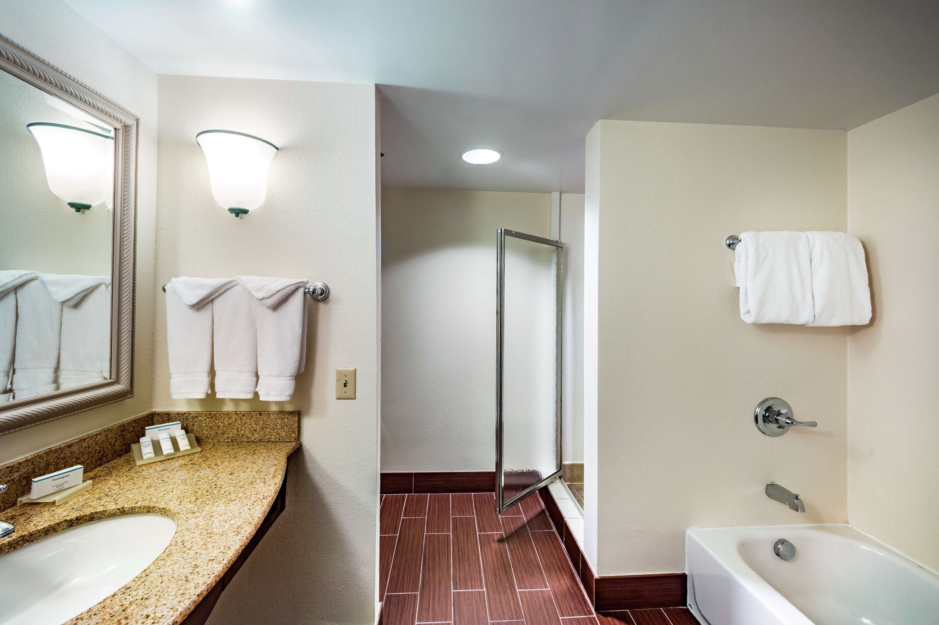 A hotel bathroom with a sink, mirror, towel rack, shower, and bathtub.