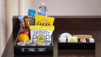 A tray with snacks and condiments including Lay's Baked chips, Skinny Pop white cheddar, and a bottle of water.