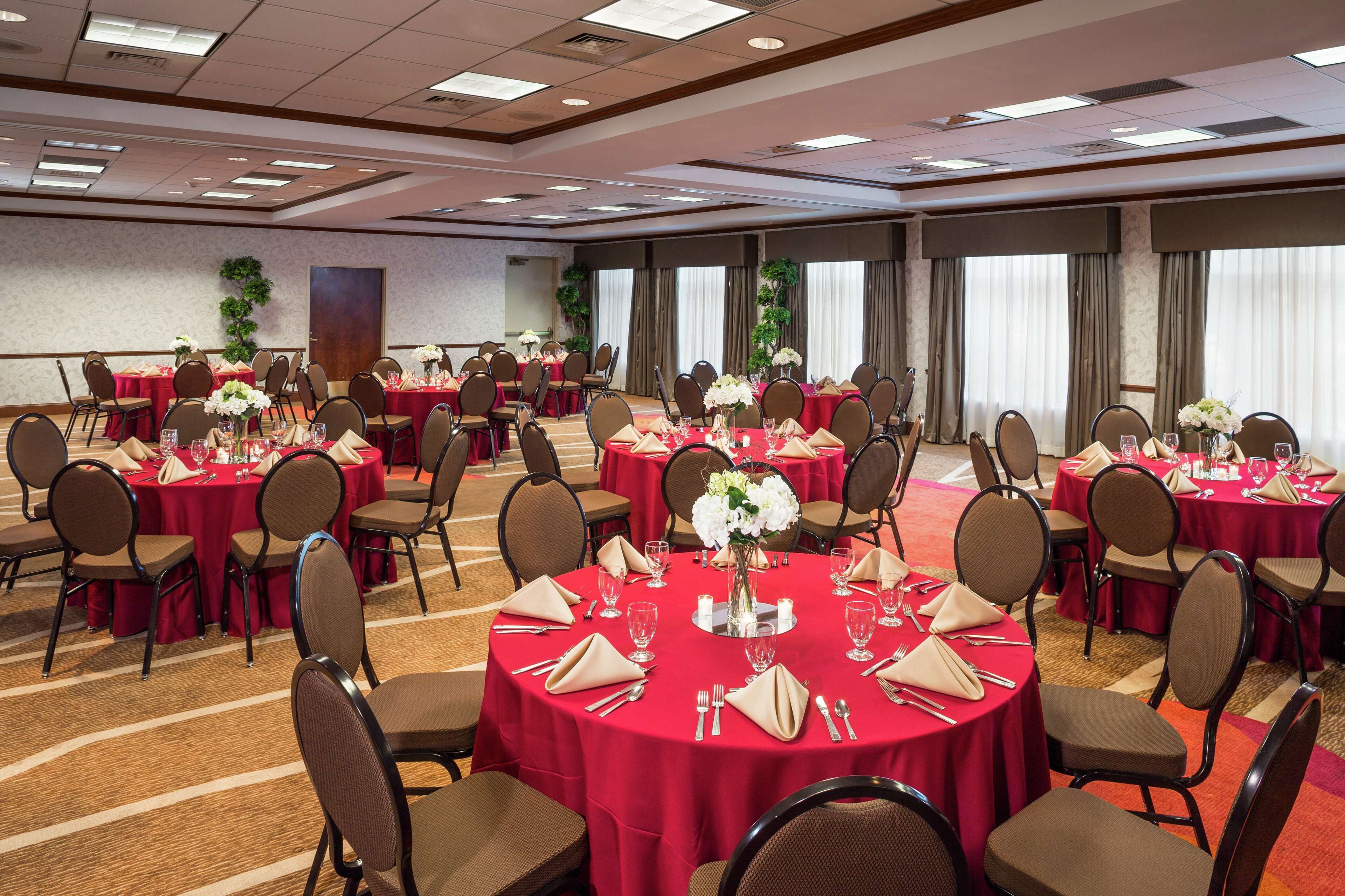 Une salle de conférence équipée de plusieurs tables dressées pour un repas, chacune étant accompagnée de chaises et de couverts.