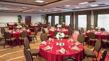 Une salle de conférence équipée de plusieurs tables dressées pour un repas, chacune étant accompagnée de chaises et de couverts.