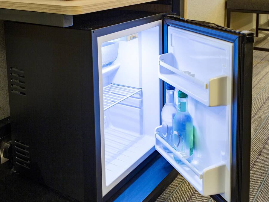 Un refrigerador compacto con un compartimento congelador, dispensador de agua y un estante.