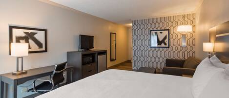 Ein Hotelzimmer mit Bett, Schreibtisch, Stuhl, Fernseher und einer Wand mit geometrischen Mustern.